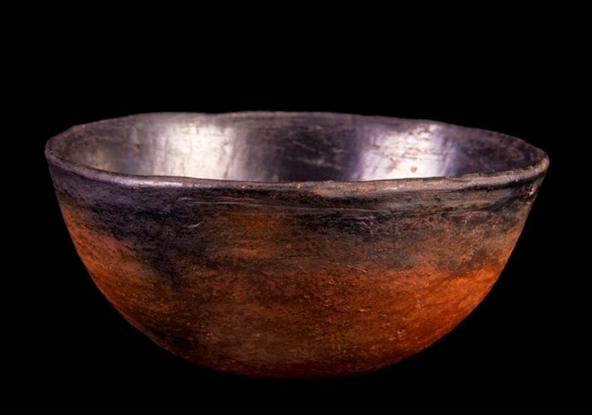 An unpatterned black and red ceramic bowl against a black background