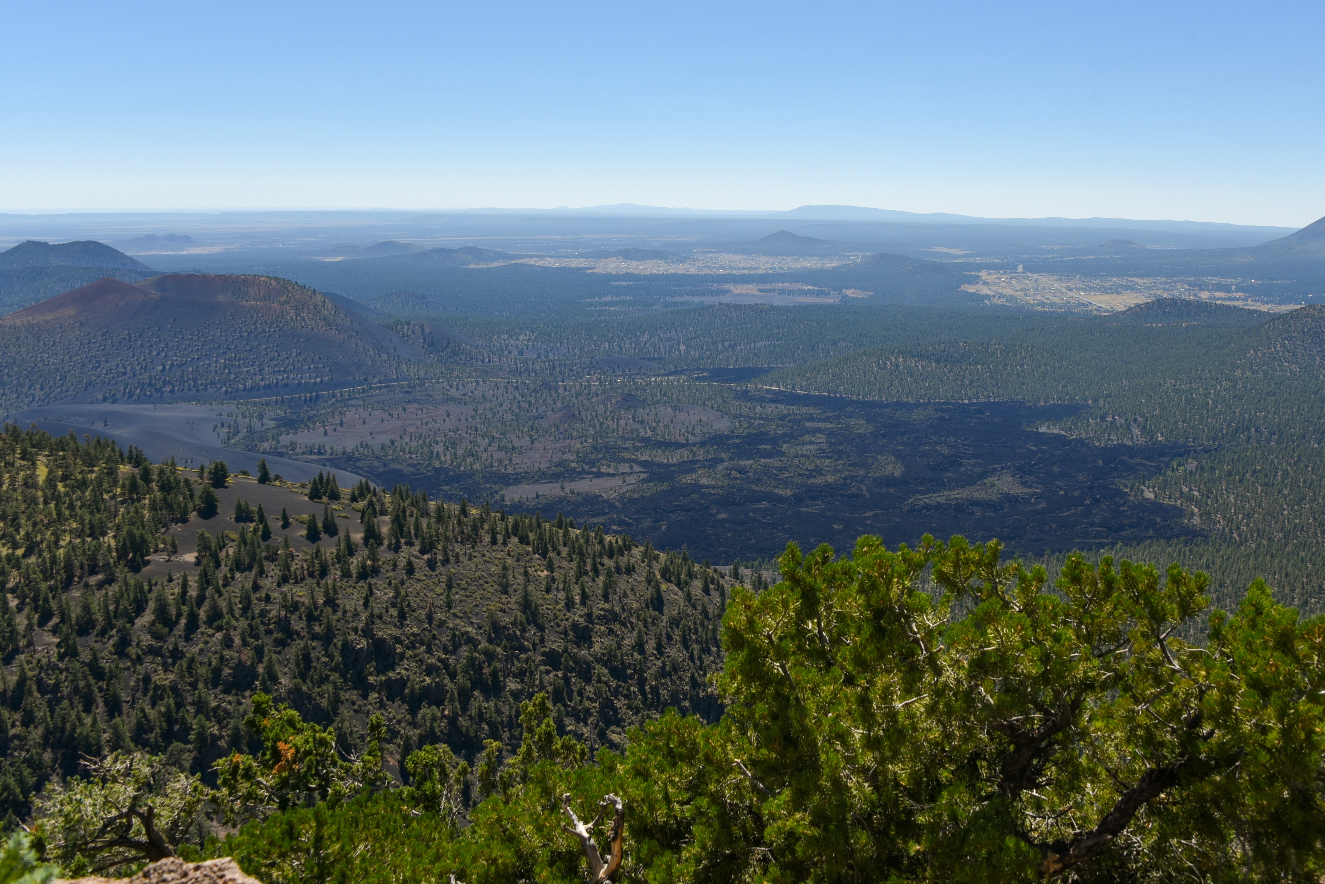 View from above of a black lava flow surrounded by green trees and small hills