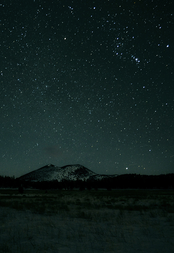 a volcanic cinder cone under a dark night sky with many stars