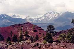 Cinder and lava formations, with snow-covered peaks in background Cinder and lava formations, with snow-covered peaks in background