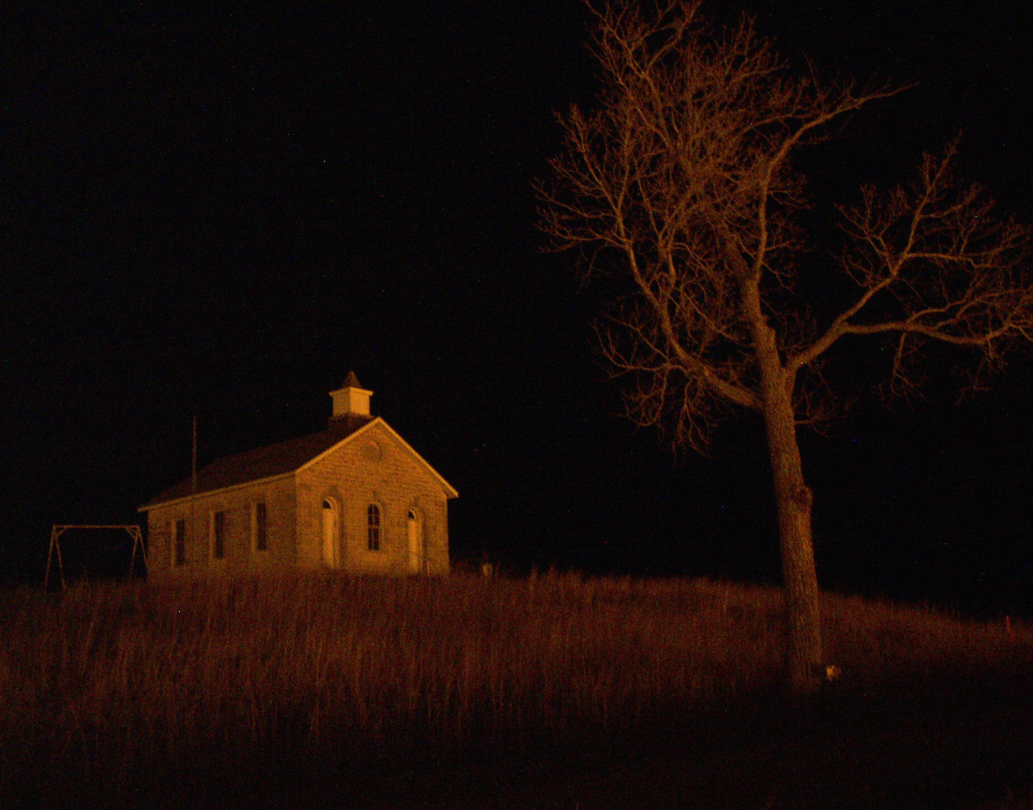 One-room schoolhouse lit up by light of a prairie fire
