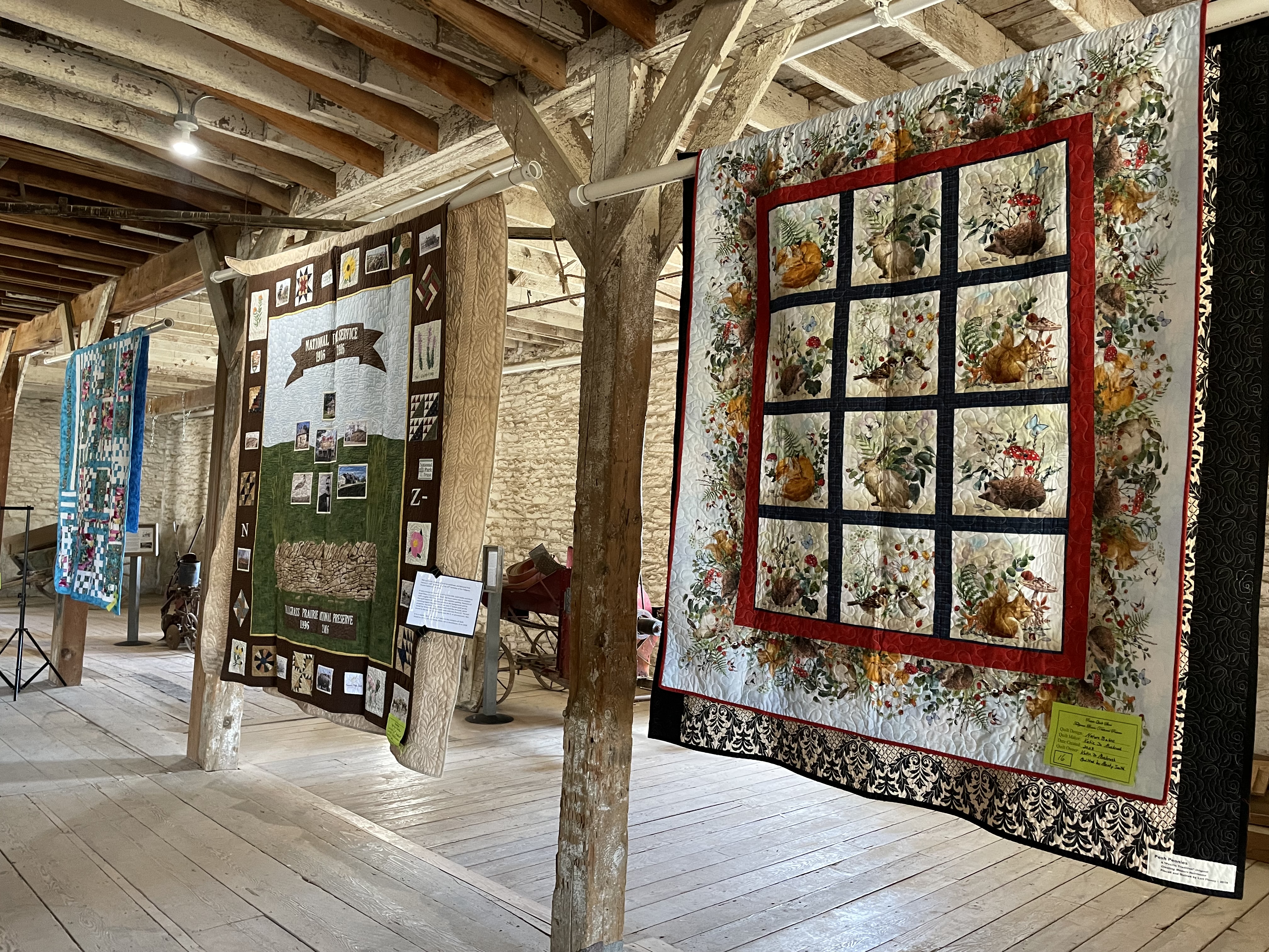 Quilts hanging among the historic posts in the 1882 limestone barn with farming machinery in the background.