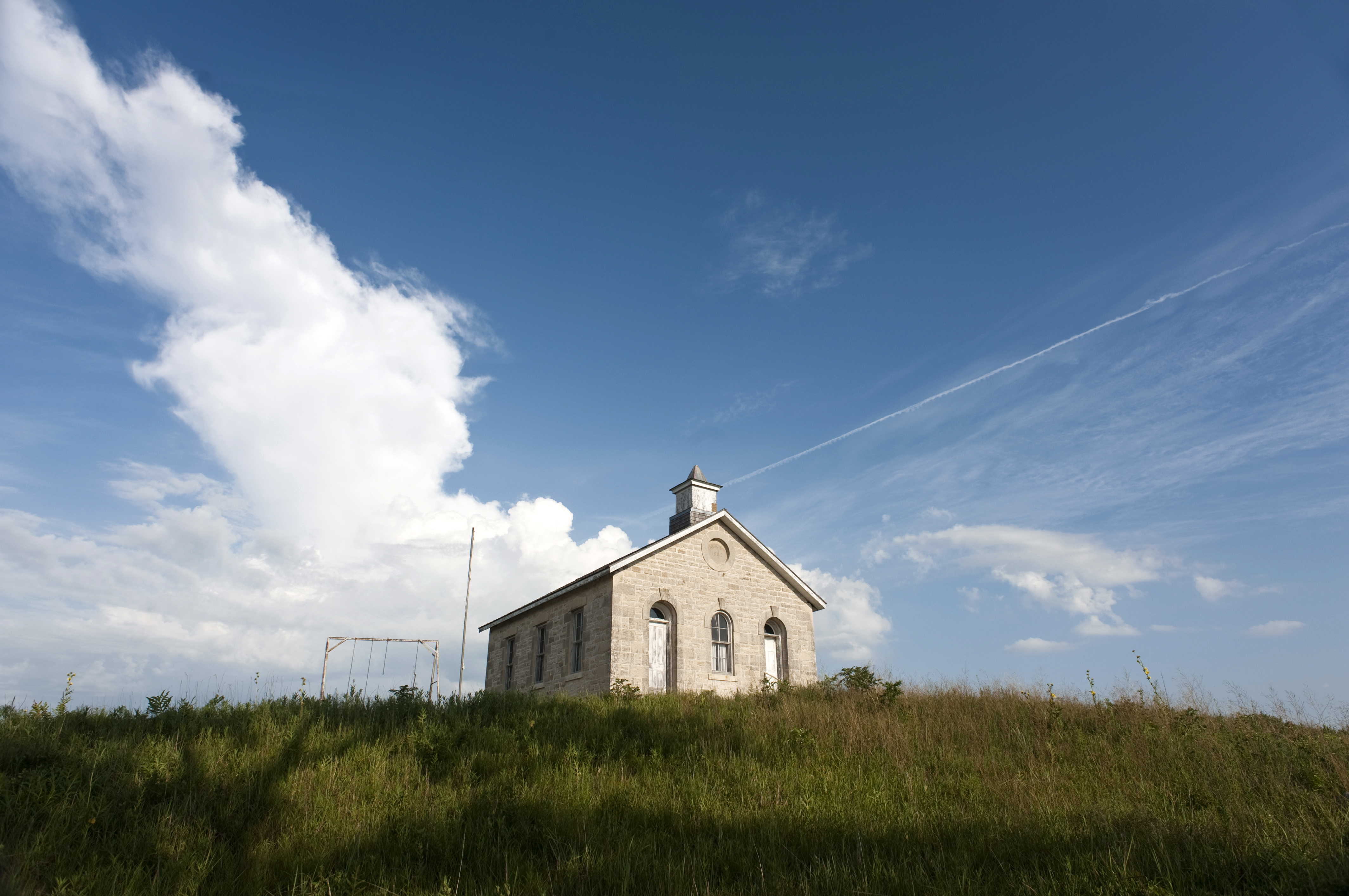 Photo of historic one room school on a hill top with blue sky and beautiful puffy clouds in the background.