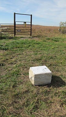 Hiking gate for crossing through pastures found behind a white cube-shaped trail marker stone.