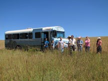 Uniformed ranger giving a bus tour on the greenish yellow prairie with blue sky behind.