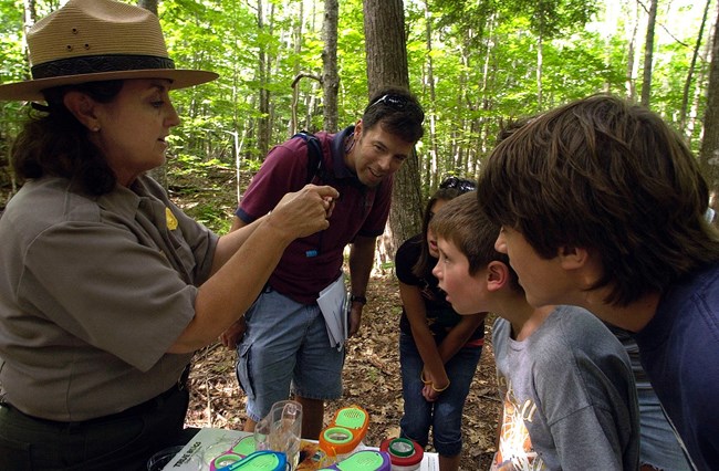 A group of children and adult watch a park ranger demonstration.