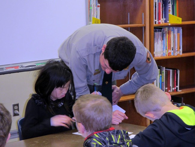 ranger leans down with students sitting in a group in the classroom