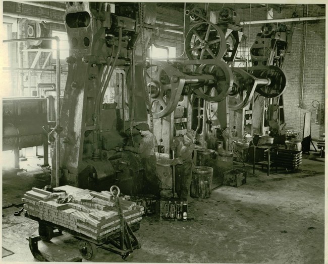 Two men working at drop forging machinery at the Armory.