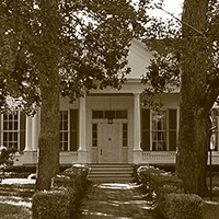 Shields Town House brick path lined with hedges leading to porch of two-story house with large windows