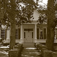 brick path lined with hedges leading to porch of two-story house with large windows