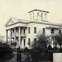 stately home with large columns across the front surrounded by treets