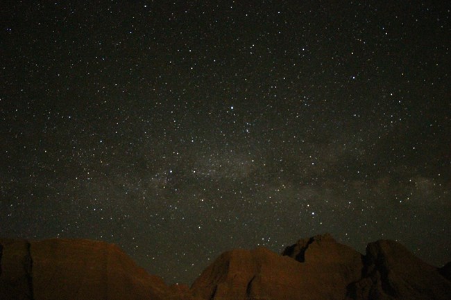 a sky filled with stars and the milky way with the tops of badlands buttes below