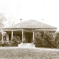 house with porch across the front partially hidden by hedges