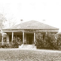 Oakland house with porch across the front partially hidden by hedges