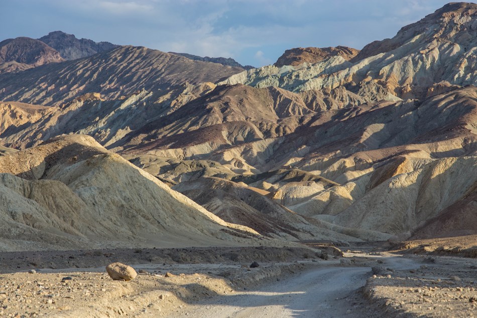 Multi-hued eroded badlands with a dirt road through them. Multi-hued eroded badlands with a dirt road through them.