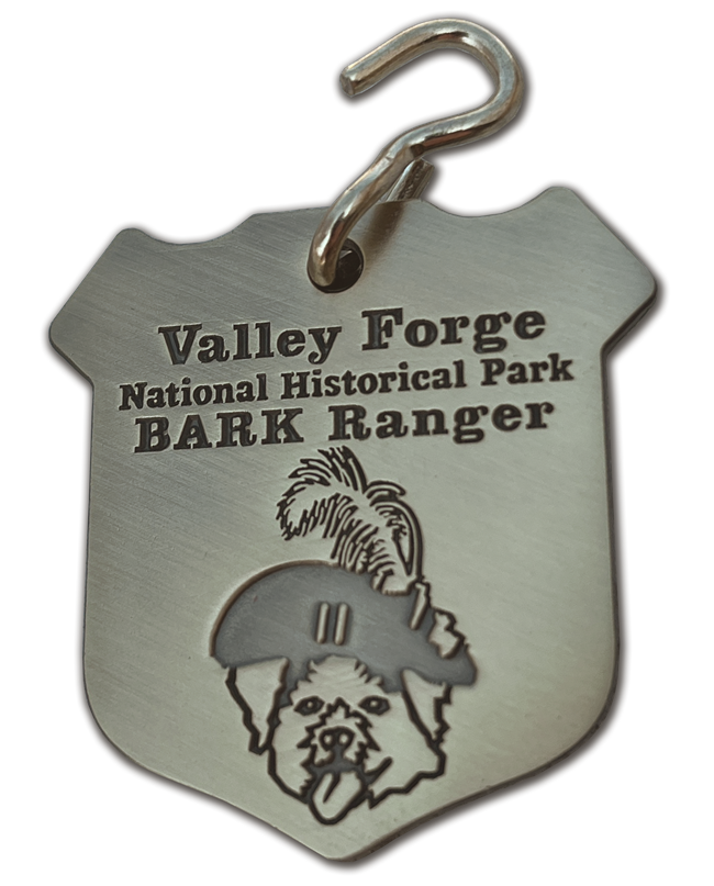 Metal dog tag in the shape of a shield. Head of a dog wearing Revolutionary War hat.