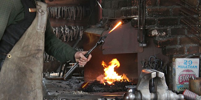 Blacksmith demonstrates at the forge Park Ranger holds hot iron near the forge during a demonstration.