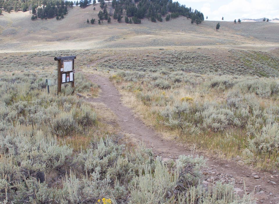Blacktail Deer Creek Trail near trailhead Trailhead sign at the start of the trail, which leads off across an open, hilly expanse of sagebrush.