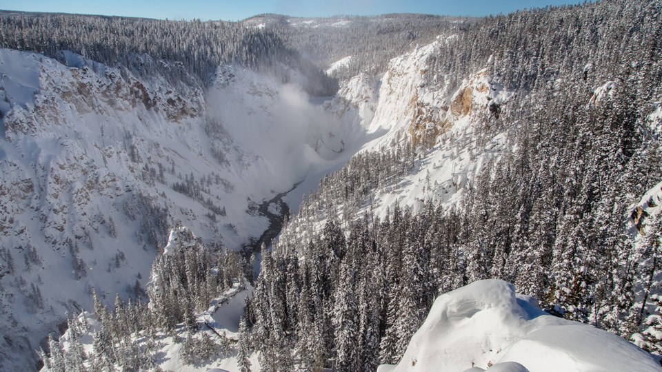 Snow covers the canyon walls and ice and mist cover the waterfall plunging into the canyon