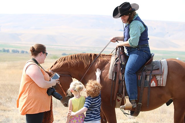 Ranger on horseback with mother and children petting the horse.