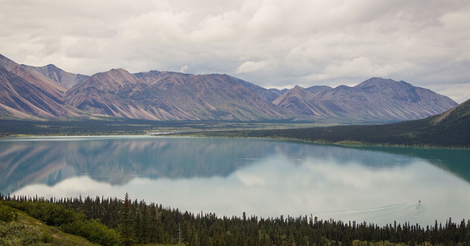 a glassy lake surrounded by colorful mountains with a small boat on the water a glassy lake surrounded by colorful mountains with a small boat on the water