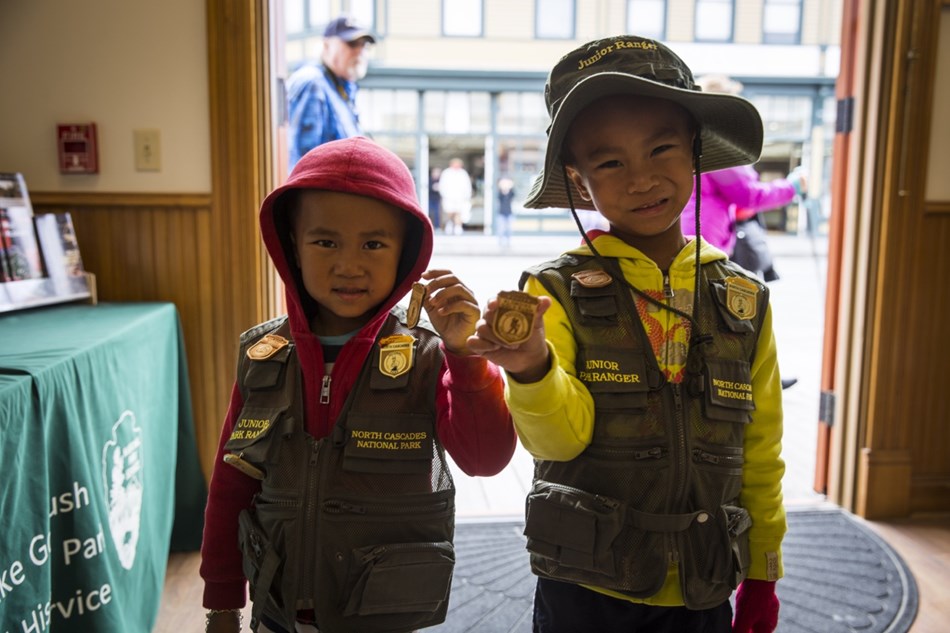 Two children in junior ranger vests display badges for the camera. Two children in junior ranger vests display badges for the camera.
