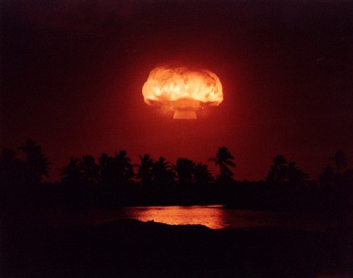 A bright orange mushroom cloud rises over a dark red sky