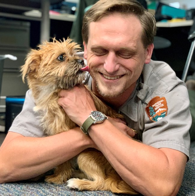 Scruffy small dog licking a park ranger's face