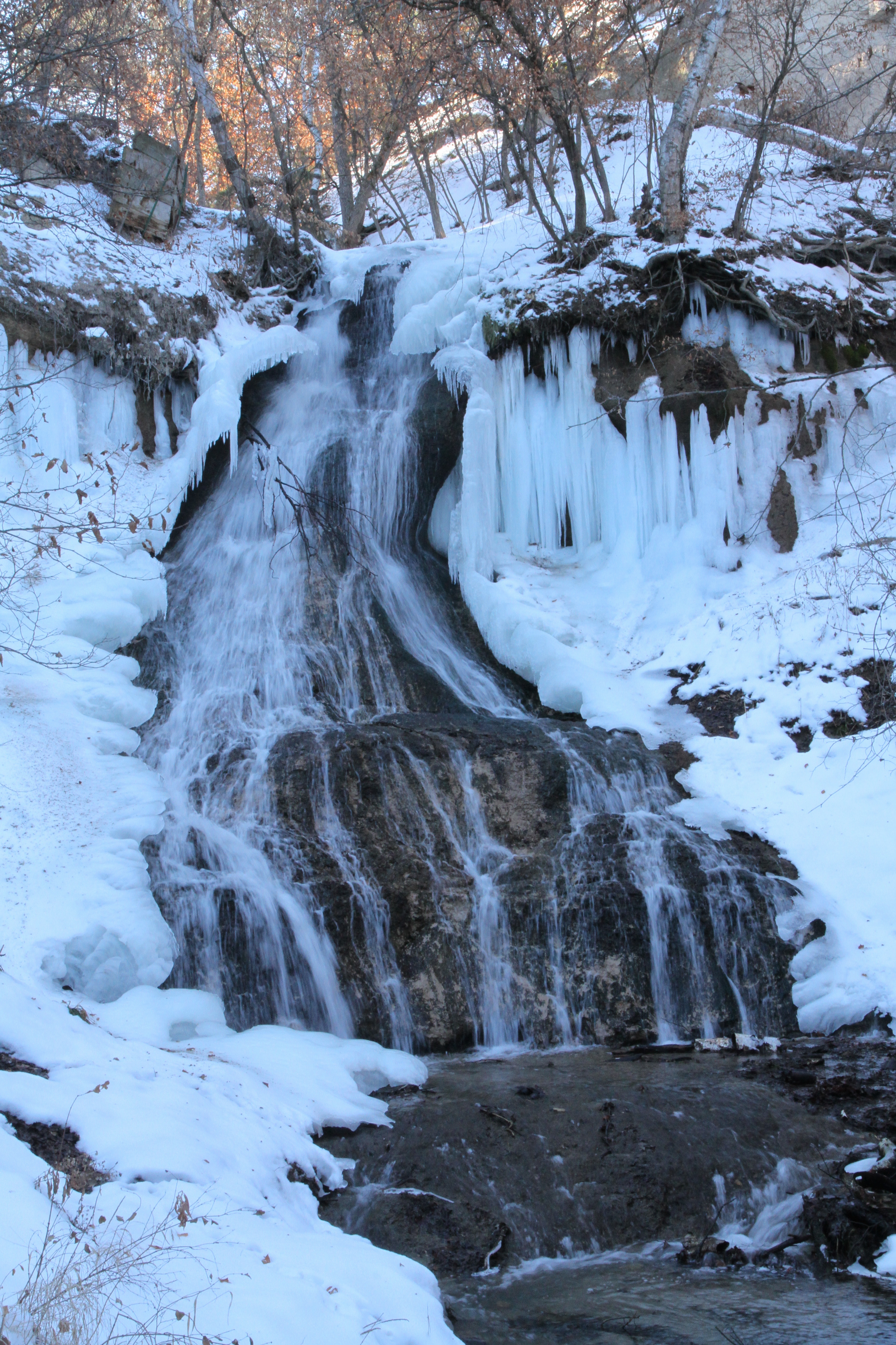 A waterfall flowing over a ledge and into a pool with snow on all sides.