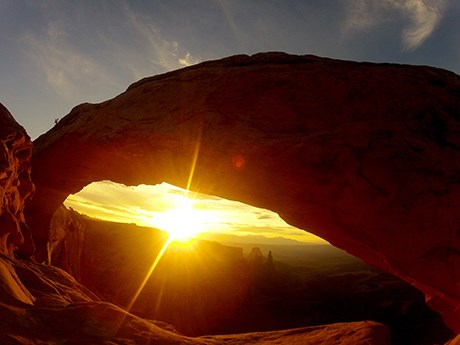 the sun's rays shine beneath a broad, silhouetted arch