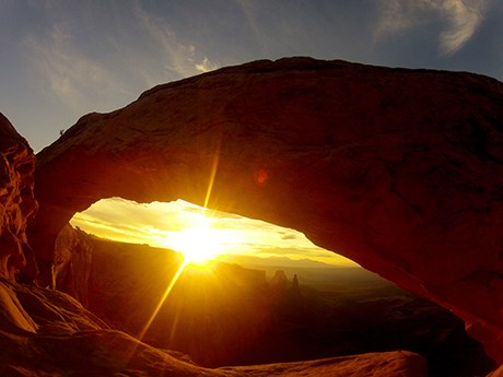MesaArch Sunrise the sun's rays shine beneath a broad, silhouetted arch