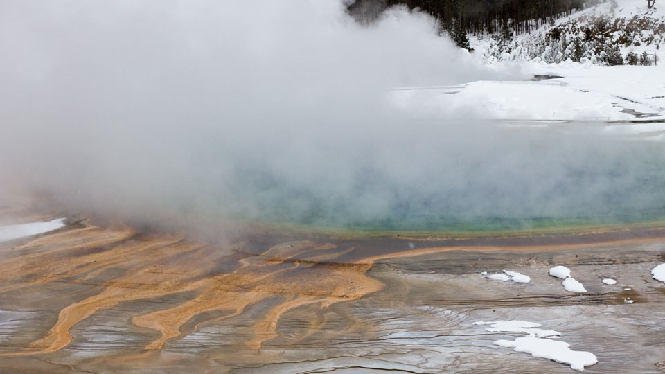 Grand Prismatic Spring in winter from the overlook. Steam rises from the prismatic pool surrounding by snow.