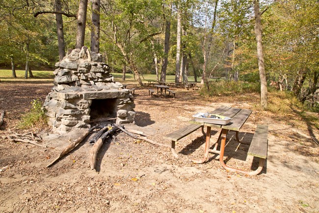 A picnic table sits beside a stone chimney grill.