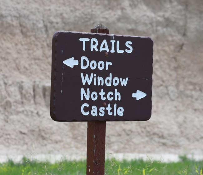 a brown sign with white text pointing to door, window, and castle trails. a brown sign with white text pointing to door, window, and castle trails.