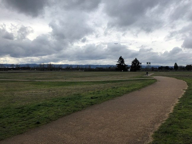 A paved trail on a cloudy day with Fort Vancouver in the background.