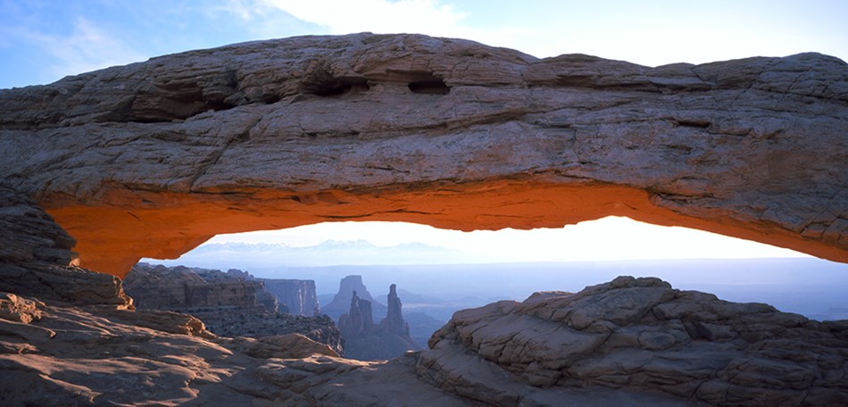 A broad stone arch with mountains and rock pinnacles in the background