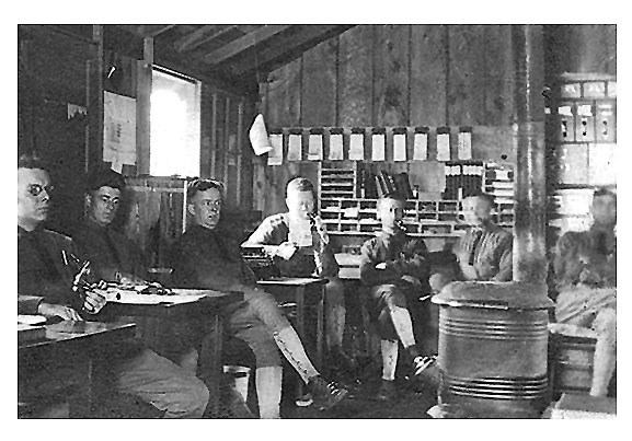 A black and white photo of soldiers sitting indoors at tables smoking.