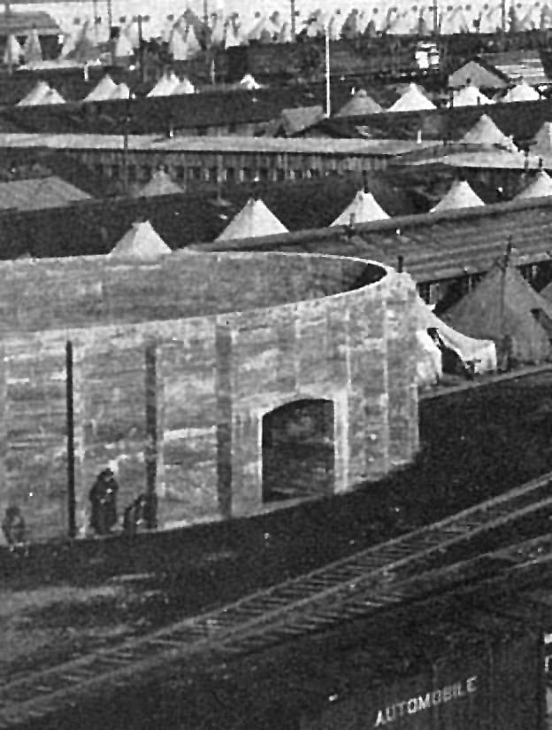 A black and white photo of a round concrete structure with white canvas tents in the background.