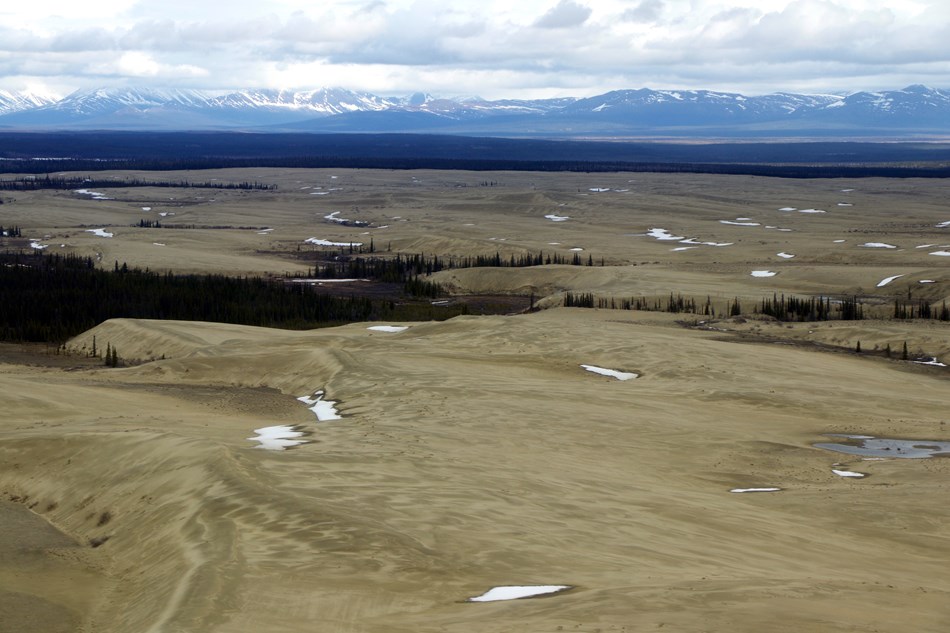 View of the sand dunes with snow patches and snow-capped mountains in the distance. View of the sand dunes with snow patches and snow-capped mountains in the distance.