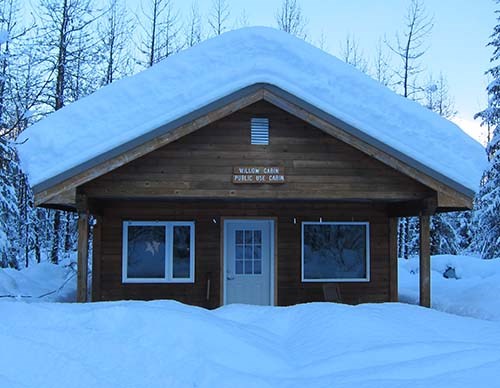 Willow Public Use Cabin Snow covered, wooden cabin.