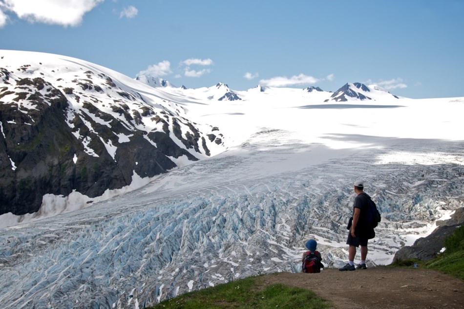 A father and son overlook a glacier and icefield with mountains in the distance. A father and son overlook a glacier and icefield with mountains in the distance.