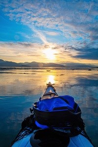 photo of the front of a sea kayak pointed towards a dramatic sunset