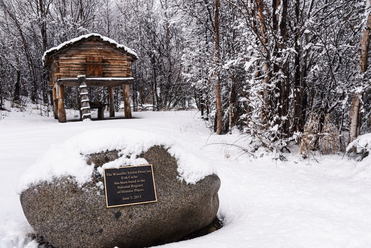 Wassillie Trefon Dena'ina Fish Cache a wooden structure with a small door on stilts in winter