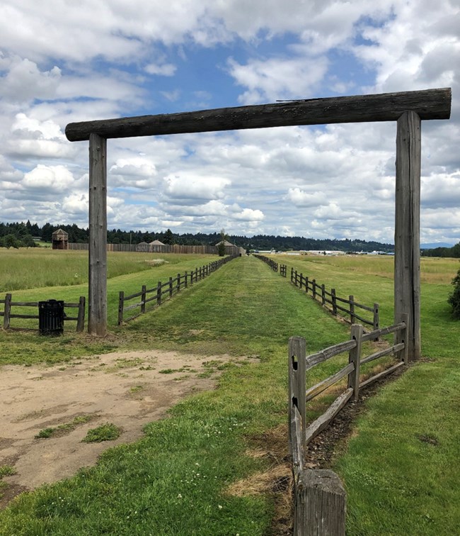 A wooden gate leading to a gravel trail. Fort Vancouver is in the background.