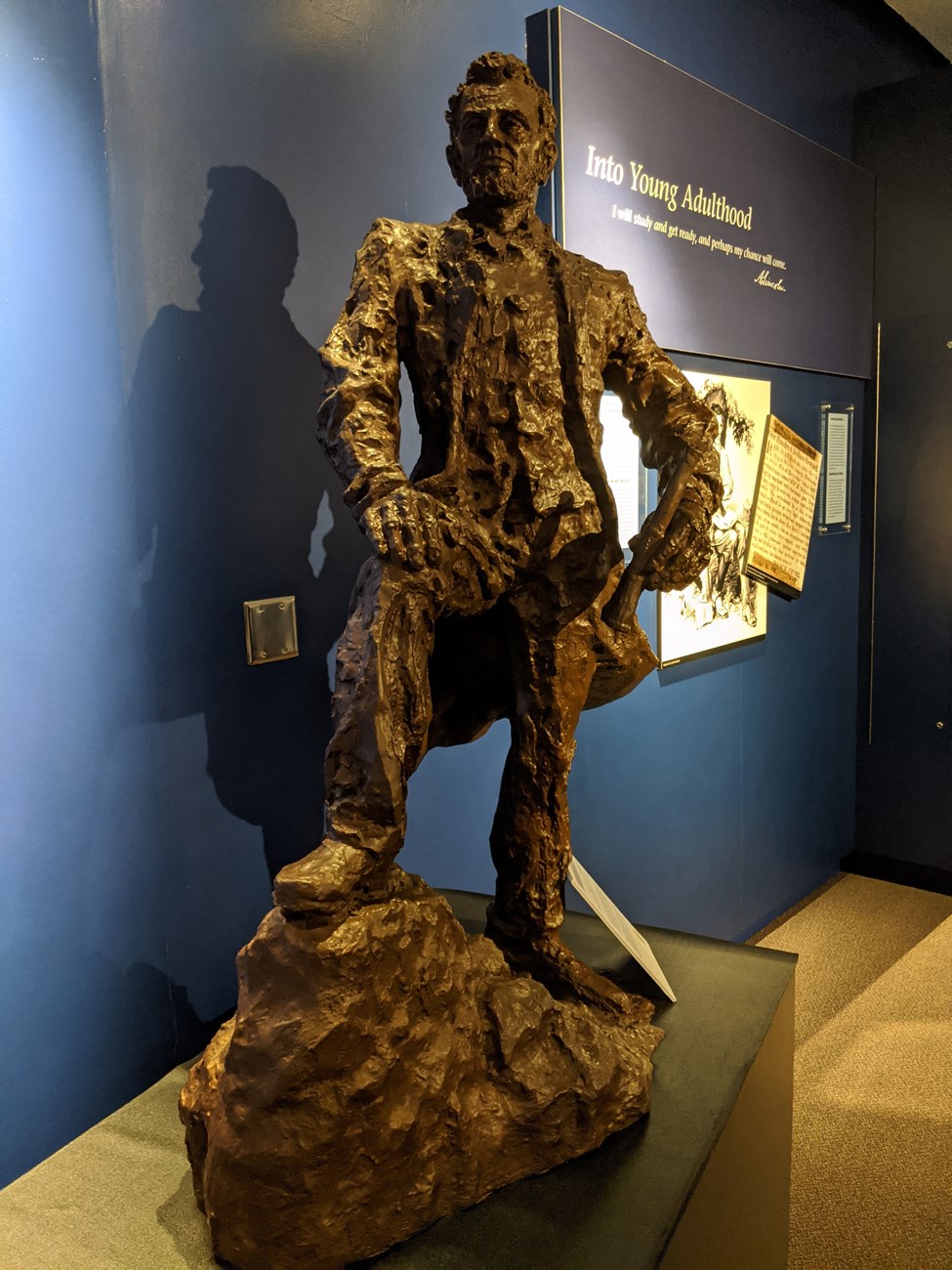 Statue of Abraham Lincoln standing on rock, right foot higher with hand on his knee.