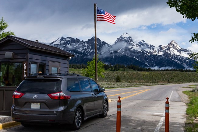 Cars wait in line at entrance station with mountains in the background.