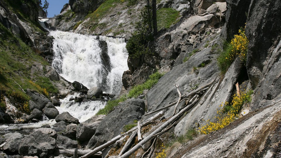 Mystic Falls Waterfall cascading down a steep river channel by some gray boulders.