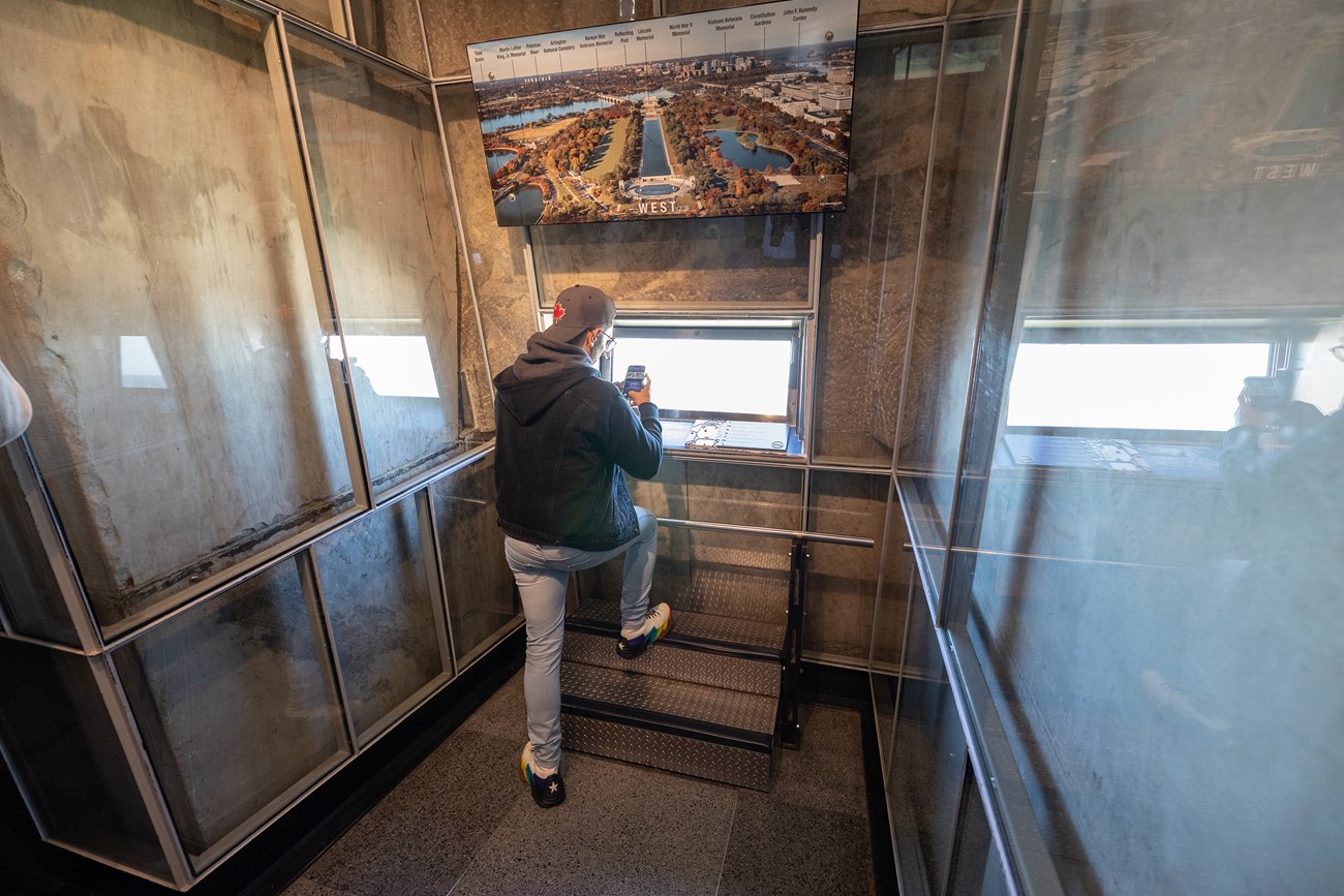 NAMA_WAMO_Stairs_20231011_KGraczyk_18 A man takes a photo from a rectangular window inside the Washington Monument.