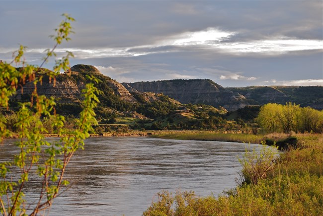 Little Missouri River flowing though prairie with buttes in background.