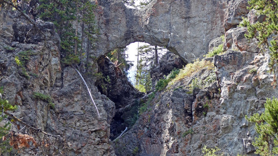 Natural Bridge in Yellowstone Gray stone rock arches over a creek drainage.